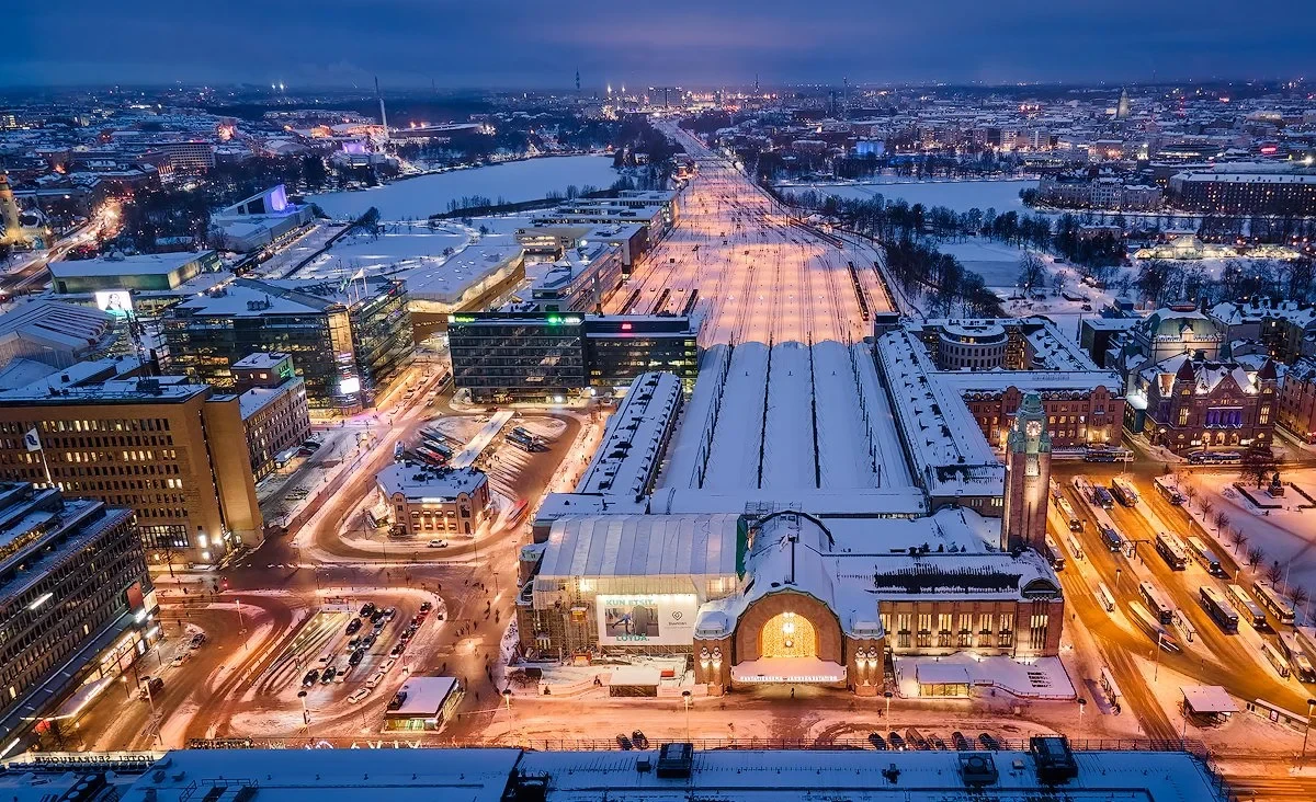 Aerial view of Helsinki Central Railway Station and surrounding cityscape at night, covered in snow.