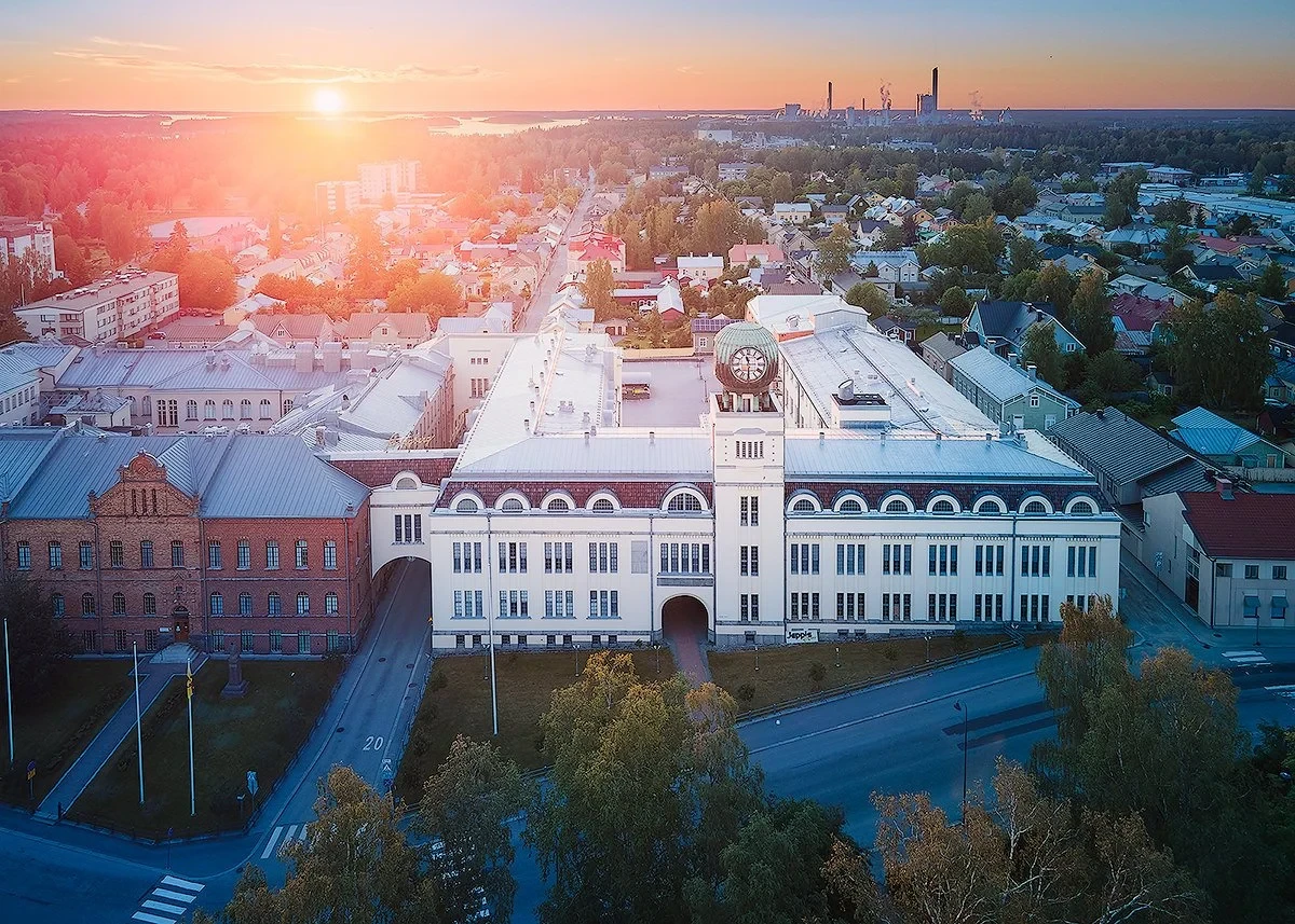 Aerial view of a large, historic building with a clock tower in a cityscape during sunset.