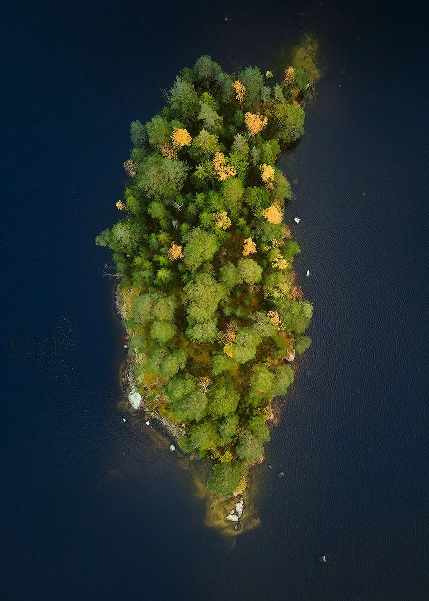 Aerial view of a small forested island in a body of water, surrounded by dark blue water.