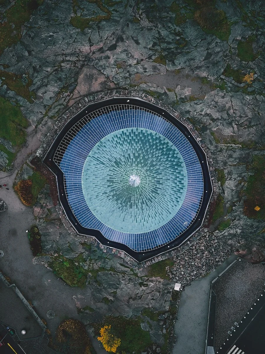 Aerial view of Temppeliaukio Church's circular roof in Helsinki, surrounded by rocky terrain.
