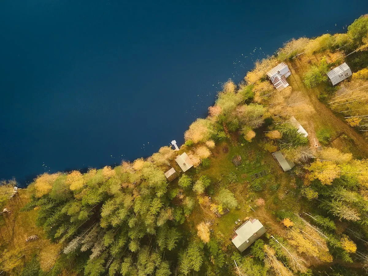 Aerial view of a lakeside area featuring several small cabins surrounded by autumn-colored trees and greenery.