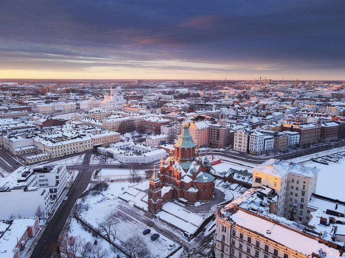Aerial view of a snow-covered cityscape with a prominent church featuring onion domes in the foreground during sunrise or sunset.