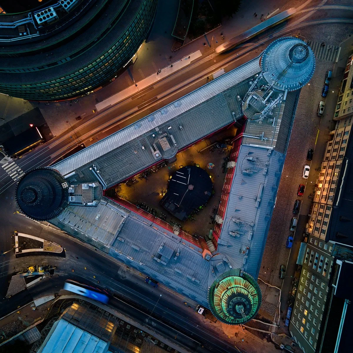 Aerial view of a triangular urban building with three distinct towers, surrounded by roads and cityscape, illuminated at night.